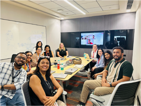 Full team seated around a table with remote colleagues on video call